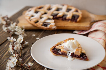 American cherry pie. A piece of  pie with a scoop of ice cream on a white plate in the foreground with a sprig of cherry blossoms. 