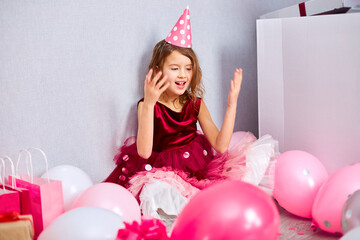 Beautiful little girl blows up multicolored confetti, having fun at home birthday party