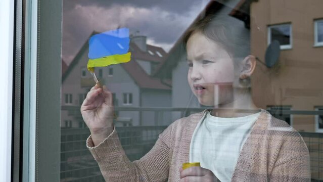 Little girl draws the flag of Ukraine on the window.