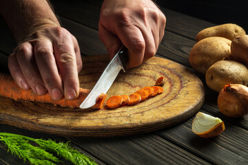 Cook cutting carrots for vegetable soup in the kitchen. Close-up of the hands of the chef during work. Carrot diet