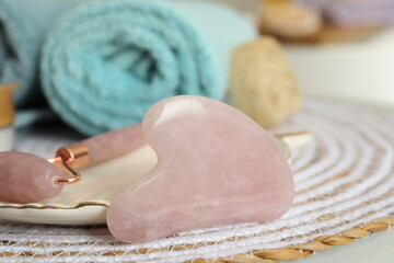 Rose quartz gua sha tool, natural face roller and towel on table in bathroom, closeup