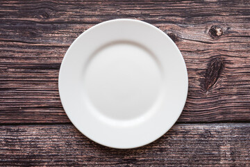 Plate on the background of a wooden tabletop. View from above. Small flat round white plate. Place for text.