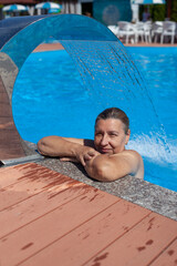 Geothermal spa center. Beautiful woman relaxes under hydro massage waterfall at tropical resort on...