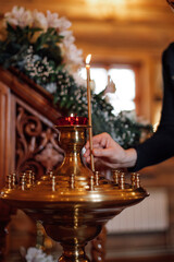 Cropped photo of woman putting burning candle on golden stand with candlesticks near artificial white flowers in orthodox church. Faith in God, religion, ceremony, praying, holiday, commemoration.