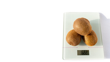 Three ripe unpeeled kiwi fruits on the scales on a white background. Kiwi is a natural dietary product, a source of vitamins and antioxidants. Healthy vegetarian food concept