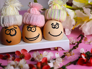Obraz na płótnie Canvas Funny Easter eggs with a close-up face and a blooming branch lie on the table on a purple background. horizontal photo