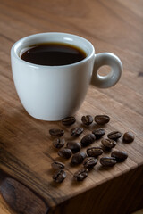White cup of coffee with coffee beans on wooden background	