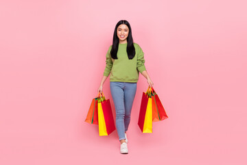 Full length photo of nice young lady go with bags wear sweater jeans footwear isolated on pink background