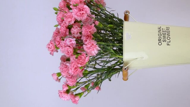 Close-up of a large number of pink carnations in a tin vase with handles on a neutral background. Vertical video. Flowers rotate around their axis on a turntable. The podium of the flower shop.
