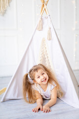 a small child girl looks out of the wigwam at home in a bright children's room and laughs © Any Grant