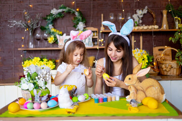 easter, mom and daughter paint Easter eggs with paint, smile and prepare for the holiday at home in the kitchen in the ears of a hare
