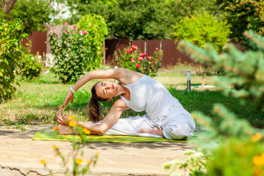 Young woman practices yoga in the summer garden - Inverted tilt of the head to the knee, parivritta Janu Shirshasana