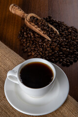 White cup of coffee with coffee beans on wooden background	