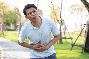 Senior man feeling stomach ache feels very painful while with park background.