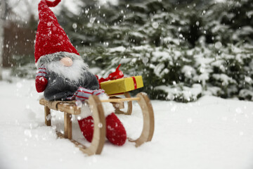Wooden sleighs with Christmas gnome and gift box on snow outdoors. Space for text