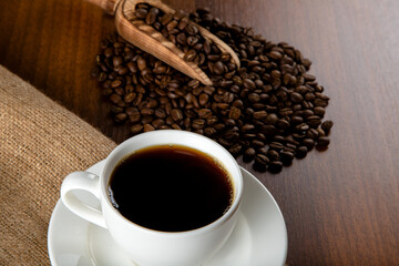 White cup of coffee with coffee beans on wooden background	