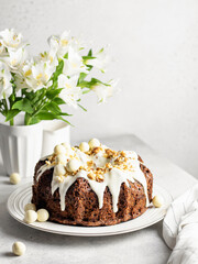 Obraz na płótnie Canvas Carrot cake with cream cheese frosting decorated with walnuts and Easter decor with flowers on white table
