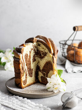 Cutted Easter cake kraffin sprinkled with powdered sugar and with white flower on a plate. Close-up of homemade two-color cake. Cruffin.