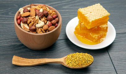 assortment of nuts and assorted dried citrus fruits and fresh floral honeycomb honey and pollen on kitchen wooden board. useful vitamin food for the human body