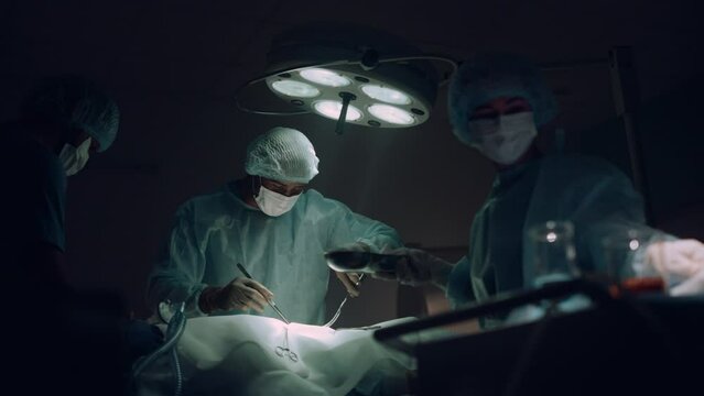 Doctors team performing surgical operation in dark hospital operating room.