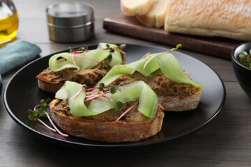 Slices of bread with delicious pate, cucumber and microgreens on wooden table, closeup