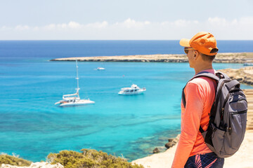 Man traveler with backpack standing on a rock and looking at amazing crystal waters of Blue lagoon in Cape Greko natural park Cyprus. © Sergey