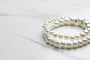 Elegant pearl bracelets on white marble table, closeup. Space for text