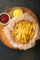 French fries. Tasty French fries server on parchment paper on wooden cutting board with tomato and cheese sauce on wooden table background. Diverse Keto Dishes. Fast food and unhealthy food concept.