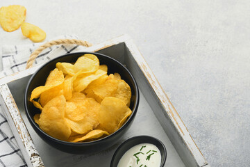 Potato chips. Fast food. Crispy potato chips ceramic black bowl with sour cream sauce and onions in wooden stand on gray kitchen table concrete background. American tradition. Hot BBQ. Top view.