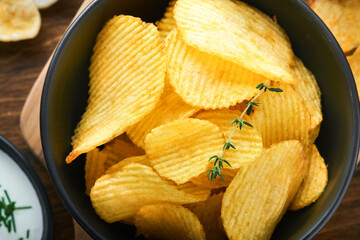 Potato corrugatedchips. Fast food. Crispy potato chips ceramic black bowl with sour cream sauce and onions in wooden stand on old kitchen table wooden background. American tradition. Hot BBQ. Top view