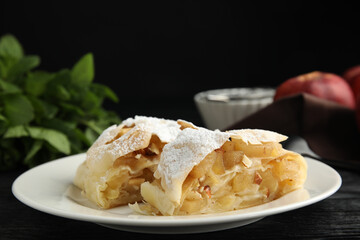 Delicious apple strudel with almonds and powdered sugar on black wooden table, closeup. Space for text