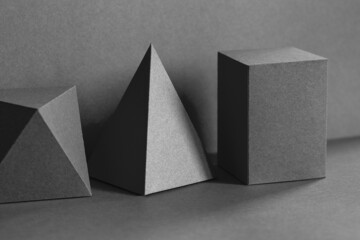 Geometrical figures still life composition. Three-dimensional prism pyramid tetrahedron rectangular cube objects on black gray background. Platonic solids figures, simplicity concept photography