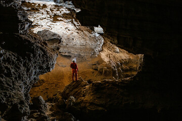 Caver man is looking through the cave gallery; speleologist - obrazy, fototapety, plakaty