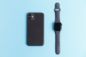 New smartwatch and smartphone. The smart watch is lying next to the mobile phone on a blue background. Modern design for high-tech gadgets and sports technology concepts. Top view