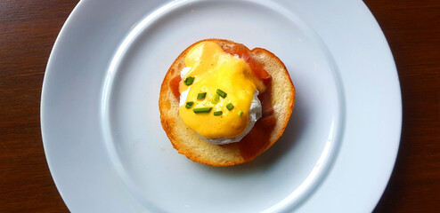 Flat ay of bread with poached egg, bacon and sweet sauce on top in dish. Top view of delicious meal of breakfast on white plate in American style. Close up food on table.