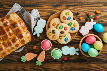 Easter hot cross buns with colored eggs Easter gingerbread rabbits and cookies over dark brown plank wooden old table background. Spring holiday baking concept. Easter table setting. Top view. Mock up