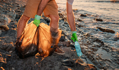 A male volunteer holding plastic bags with garbage and pick ups plastic bottle. Close up. The...