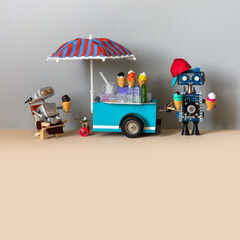 Mobile ice cream lemonade shop. Toy cart with a big umbrella, robot shopman holds waffle cones of...
