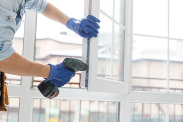 handyman adjusting white pvc plastic window indoors. worker using screwdriver to repair upvc window. homework maintenance.