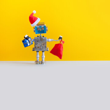 Robotic Christmas New Year greeting card. Happy Santa Claus robot with a bag of Xmas gifts on yellow gray background. Winter holidays poster creative design toy. copy space