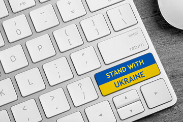 Button in colors of Ukrainian flag with phrase Stand With Ukraine on keyboard, closeup view