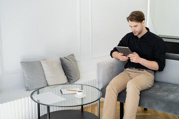 young man using digital tablet near coffee table in living room.