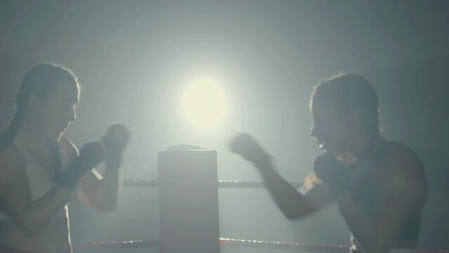 Young female boxers fighting while training together in boxing gym in the dark. Athletic women practicing punches, self-defense and dodging techniques. Sport, boxing concept