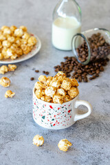 A glass of appetizing sweet milk coffee with creamy foam topped with caramel crunchy popcorn on a gray stone background. Selective focus.