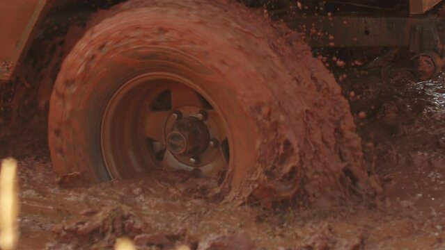 Wheel of SUV turns back trying to get out of mud pit, splashing everything around, closeup. Car is stuck on off road and is trying to leave
