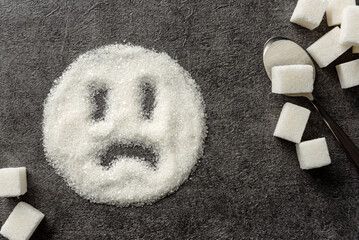 A sad smiley drawn on a pile of sugar. Sugar harm concept.