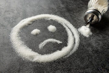 Sad emoticon drawn with sugar on the table.