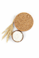 Ripe wheat ears, wheat grain and flour in a wooden bowl on white background. Top view