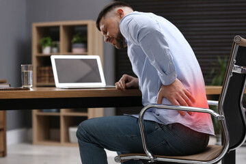 Man suffering from back pain while working with laptop in office. Symptom of poor posture - obrazy, fototapety, plakaty