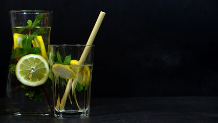 Water carafe with lemon and mint and bamboo straw against dark background